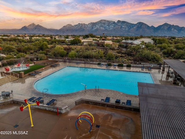 pool at dusk featuring a mountain view and a patio area