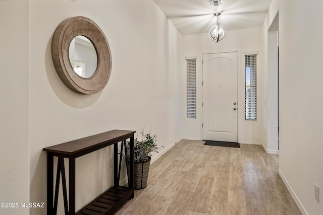 foyer entrance with light wood-type flooring, visible vents, baseboards, and an inviting chandelier