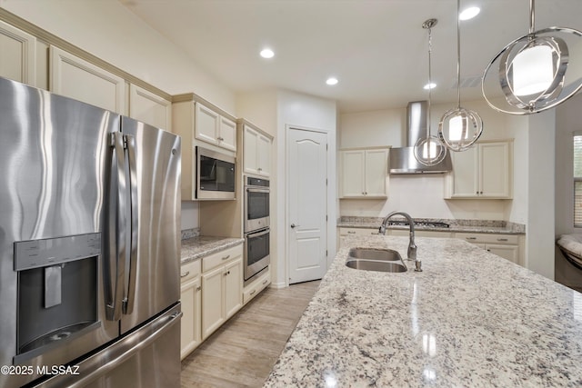 kitchen with wall chimney exhaust hood, sink, hanging light fixtures, appliances with stainless steel finishes, and cream cabinets