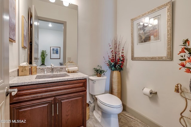 half bathroom with baseboards, vanity, and toilet