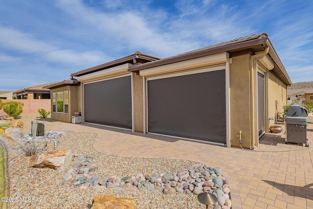 view of front facade featuring decorative driveway, a patio, stucco siding, fence, and a garage