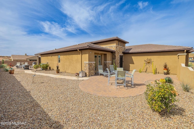 rear view of house with stone siding, a patio area, fence, and stucco siding