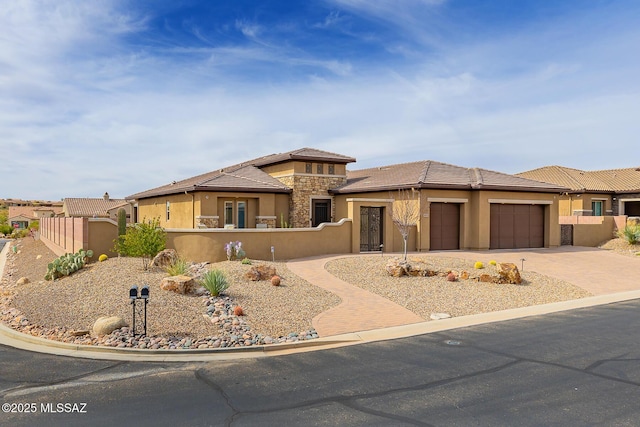 prairie-style home featuring driveway, a garage, stone siding, a tile roof, and fence private yard