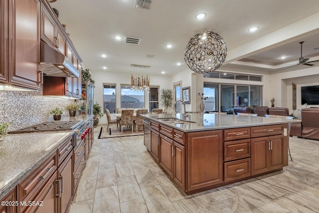 kitchen with decorative light fixtures, a kitchen island with sink, a sink, light stone countertops, and under cabinet range hood