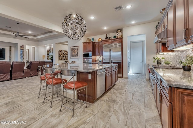 kitchen featuring under cabinet range hood, visible vents, open floor plan, a large island, and dark stone counters