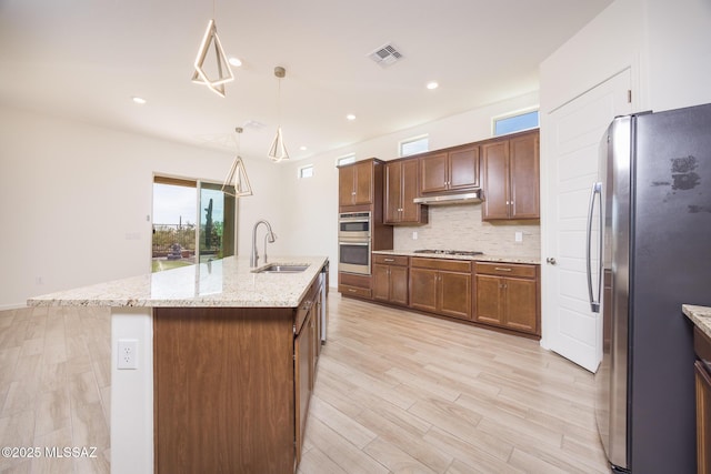 kitchen featuring decorative light fixtures, sink, backsplash, a kitchen island with sink, and stainless steel appliances