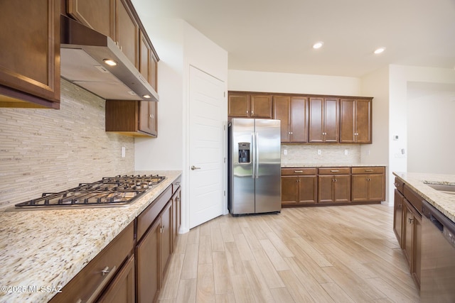 kitchen featuring light stone counters, stainless steel appliances, tasteful backsplash, and light wood-type flooring