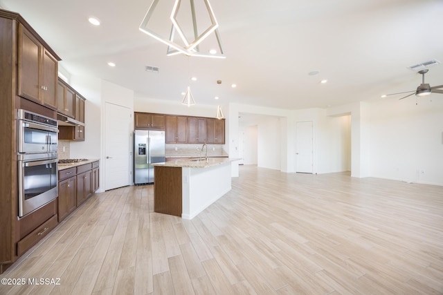 kitchen with sink, decorative backsplash, stainless steel appliances, light stone countertops, and a center island with sink