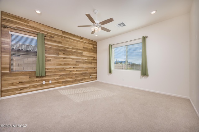 carpeted empty room with ceiling fan and wooden walls