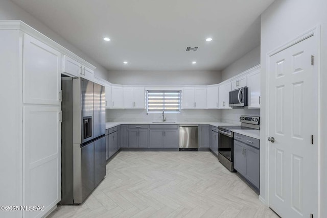 kitchen with stainless steel appliances, white cabinetry, gray cabinets, and light parquet flooring