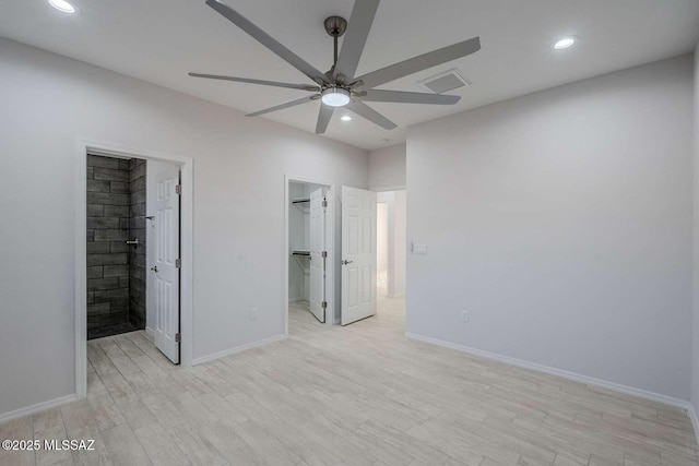 unfurnished bedroom featuring ensuite bathroom, a walk in closet, light wood-type flooring, a closet, and ceiling fan