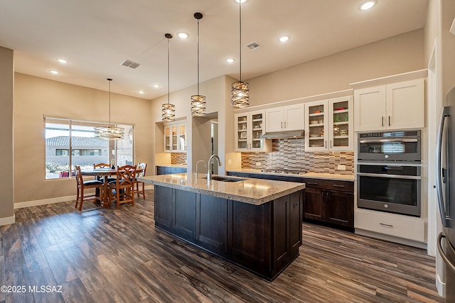 kitchen with an island with sink, light stone countertops, sink, and pendant lighting