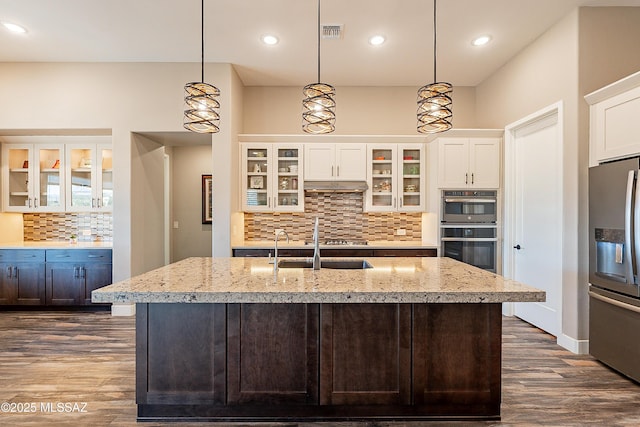 kitchen with stainless steel appliances, hanging light fixtures, and a center island with sink