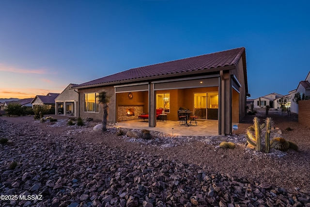 back house at dusk with a fireplace and a patio area