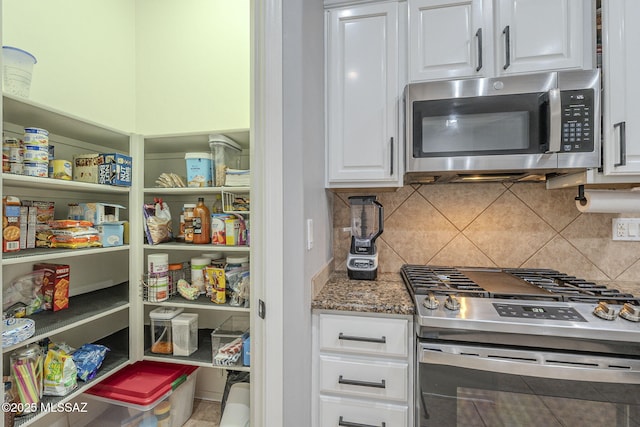 kitchen with tasteful backsplash, dark stone counters, white cabinets, and appliances with stainless steel finishes