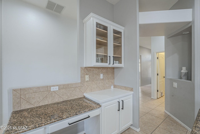 kitchen with light tile patterned flooring, dark stone counters, backsplash, and white cabinets