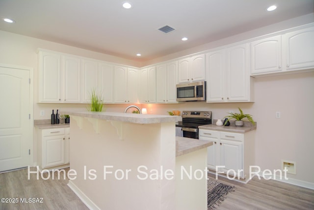 kitchen with a breakfast bar, white cabinets, a center island, stainless steel appliances, and light wood-type flooring