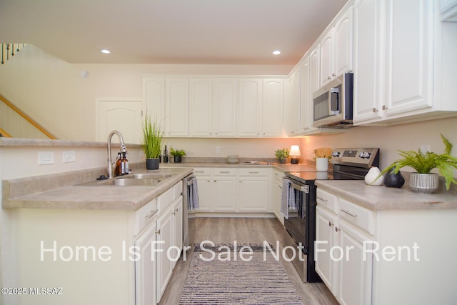 kitchen with white cabinetry, stainless steel appliances, sink, and light wood-type flooring