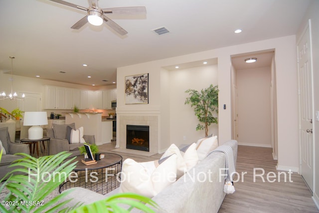 living room featuring a tiled fireplace, ceiling fan, and light hardwood / wood-style floors