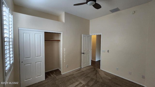 unfurnished bedroom with ceiling fan, dark carpet, and a closet