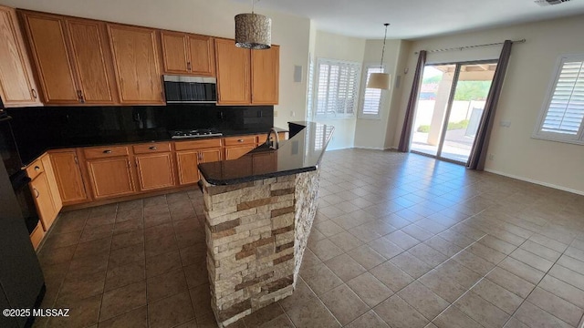 kitchen with backsplash, decorative light fixtures, black gas stovetop, and dark tile patterned flooring