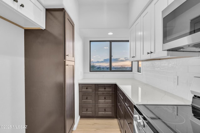 kitchen with light hardwood / wood-style flooring, dark brown cabinets, stainless steel appliances, white cabinets, and decorative backsplash