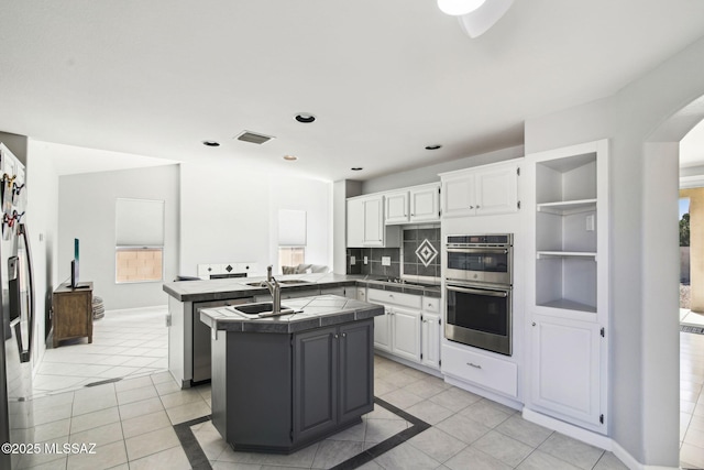 kitchen with light tile patterned floors, white cabinetry, stainless steel appliances, tile counters, and a kitchen island