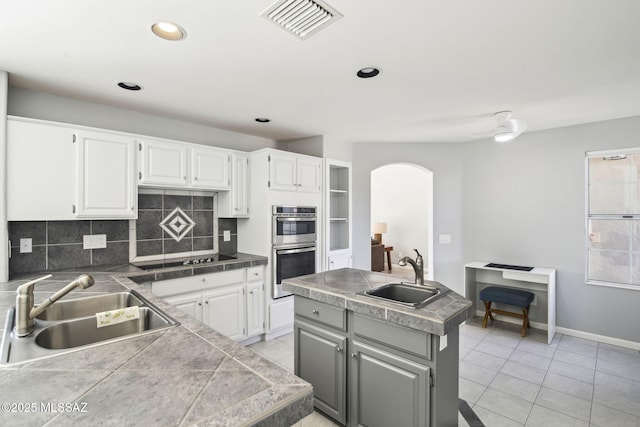 kitchen with white cabinetry, stainless steel double oven, sink, and a kitchen island with sink