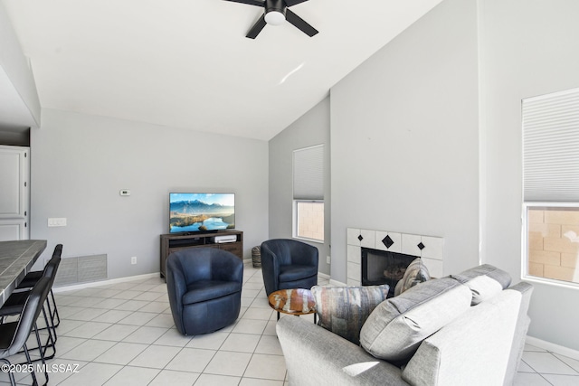 living room featuring a tiled fireplace, light tile patterned flooring, high vaulted ceiling, and ceiling fan