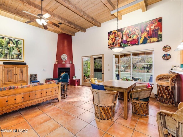 dining room with beam ceiling, a towering ceiling, a fireplace, wooden ceiling, and tile patterned floors