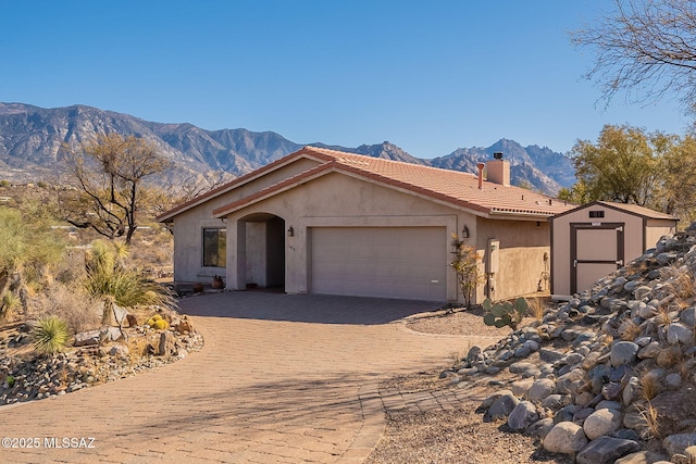 view of front of home with decorative driveway, a chimney, stucco siding, an attached garage, and a mountain view