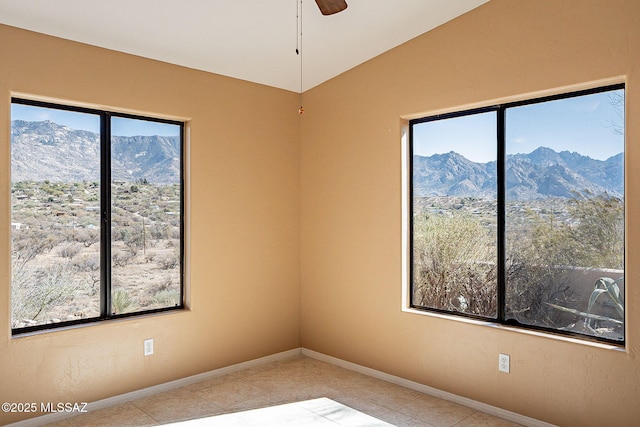 unfurnished room with a healthy amount of sunlight, baseboards, a mountain view, and ceiling fan