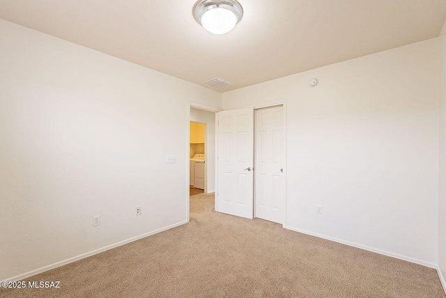 unfurnished bedroom with washer / clothes dryer and light colored carpet