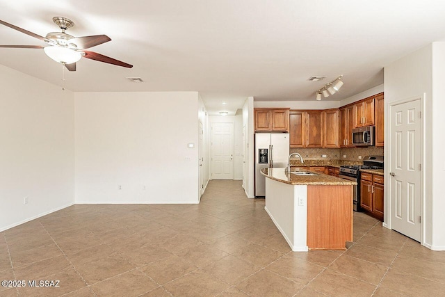 kitchen with appliances with stainless steel finishes, an island with sink, light stone countertops, decorative backsplash, and sink