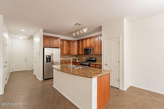 kitchen featuring a center island with sink, sink, tasteful backsplash, stone counters, and appliances with stainless steel finishes