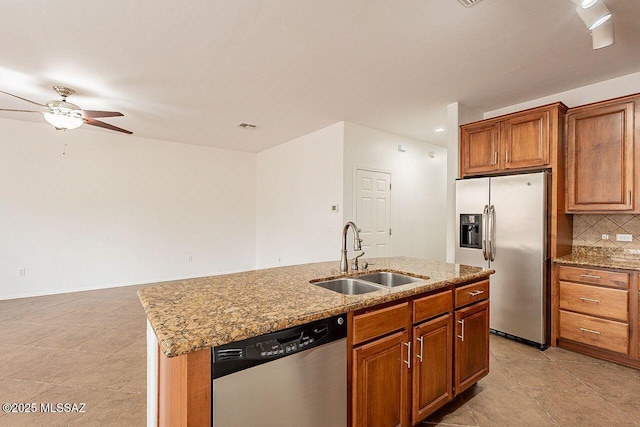 kitchen featuring a center island with sink, sink, light stone counters, stainless steel appliances, and decorative backsplash