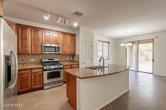 kitchen featuring stainless steel appliances, light stone counters, decorative light fixtures, sink, and a kitchen island with sink