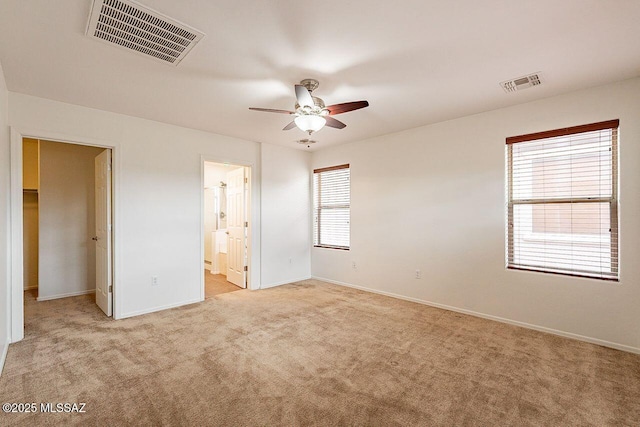 unfurnished bedroom featuring light carpet, ceiling fan, ensuite bathroom, and a walk in closet