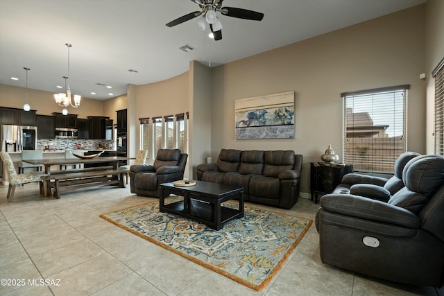 tiled living room with a towering ceiling, ceiling fan with notable chandelier, and a wealth of natural light