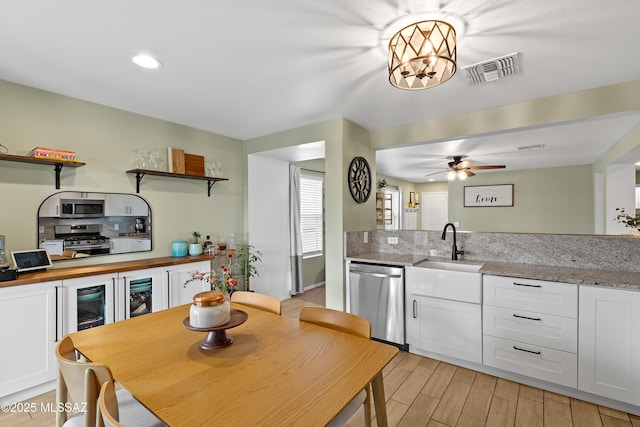 kitchen featuring sink, white cabinetry, light wood-type flooring, stainless steel appliances, and light stone countertops