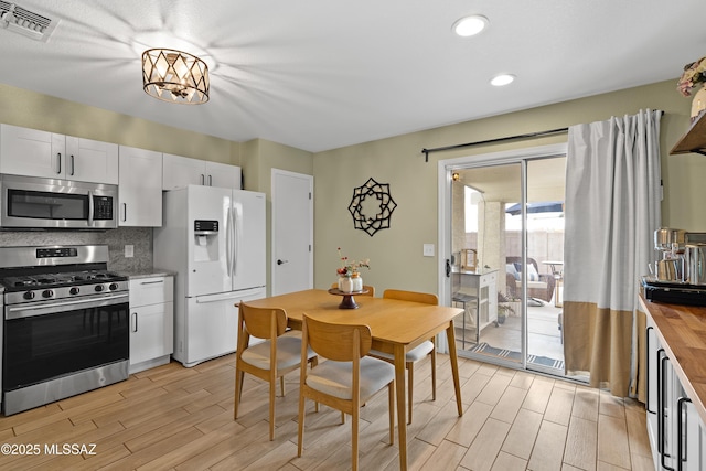 kitchen with tasteful backsplash, white cabinetry, butcher block counters, a notable chandelier, and stainless steel appliances