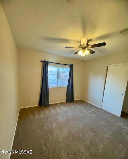 empty room featuring dark colored carpet, ceiling fan, and a textured ceiling