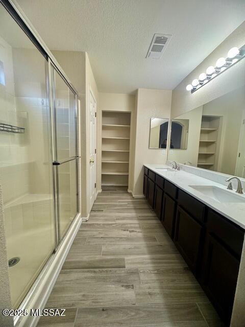 bathroom with walk in shower, built in shelves, a textured ceiling, vanity, and hardwood / wood-style floors