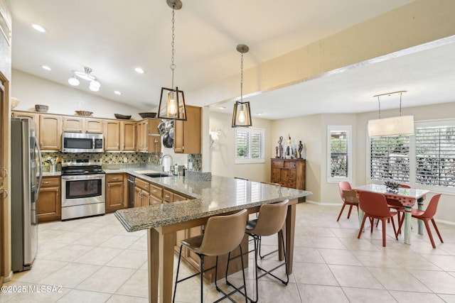 kitchen featuring a kitchen bar, sink, stone countertops, appliances with stainless steel finishes, and kitchen peninsula