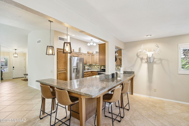 kitchen featuring a breakfast bar, dark stone countertops, light tile patterned floors, kitchen peninsula, and stainless steel appliances