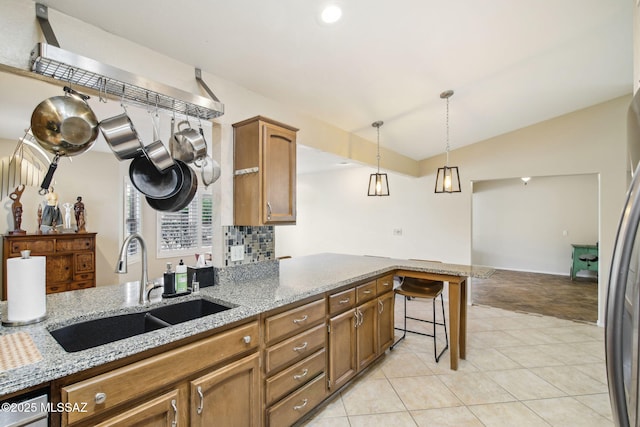 kitchen featuring vaulted ceiling, a breakfast bar, decorative light fixtures, sink, and light stone countertops