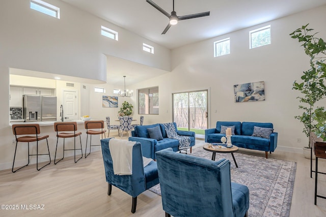 living room featuring sink, ceiling fan with notable chandelier, light hardwood / wood-style floors, and a towering ceiling