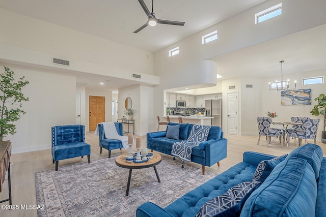 living room with a wealth of natural light, a towering ceiling, ceiling fan with notable chandelier, and light hardwood / wood-style floors