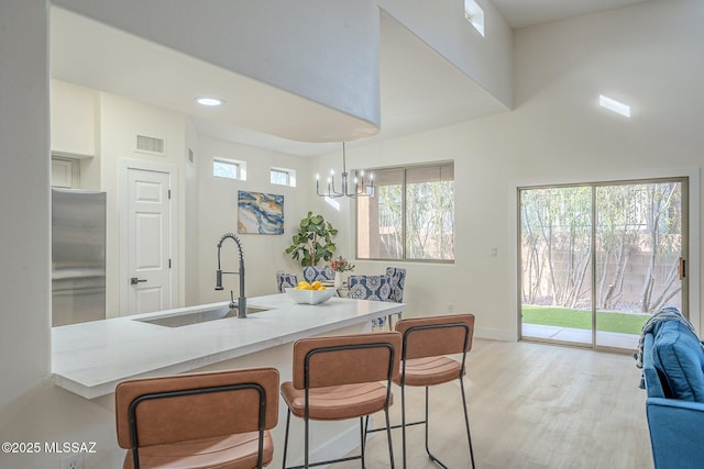 kitchen with sink, built in refrigerator, decorative light fixtures, a kitchen breakfast bar, and light hardwood / wood-style floors