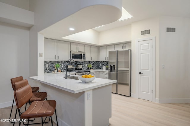 kitchen featuring a breakfast bar, sink, gray cabinetry, kitchen peninsula, and stainless steel appliances